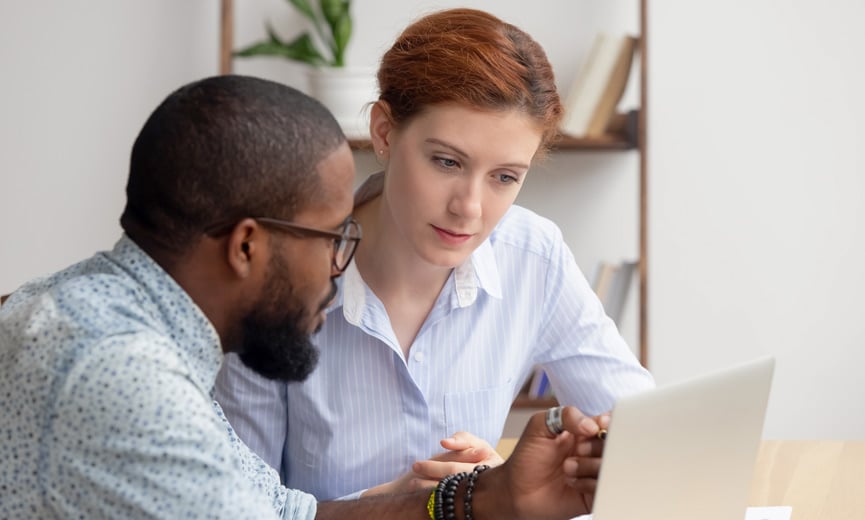 A business owner helping an employee at a laptop in an office setting