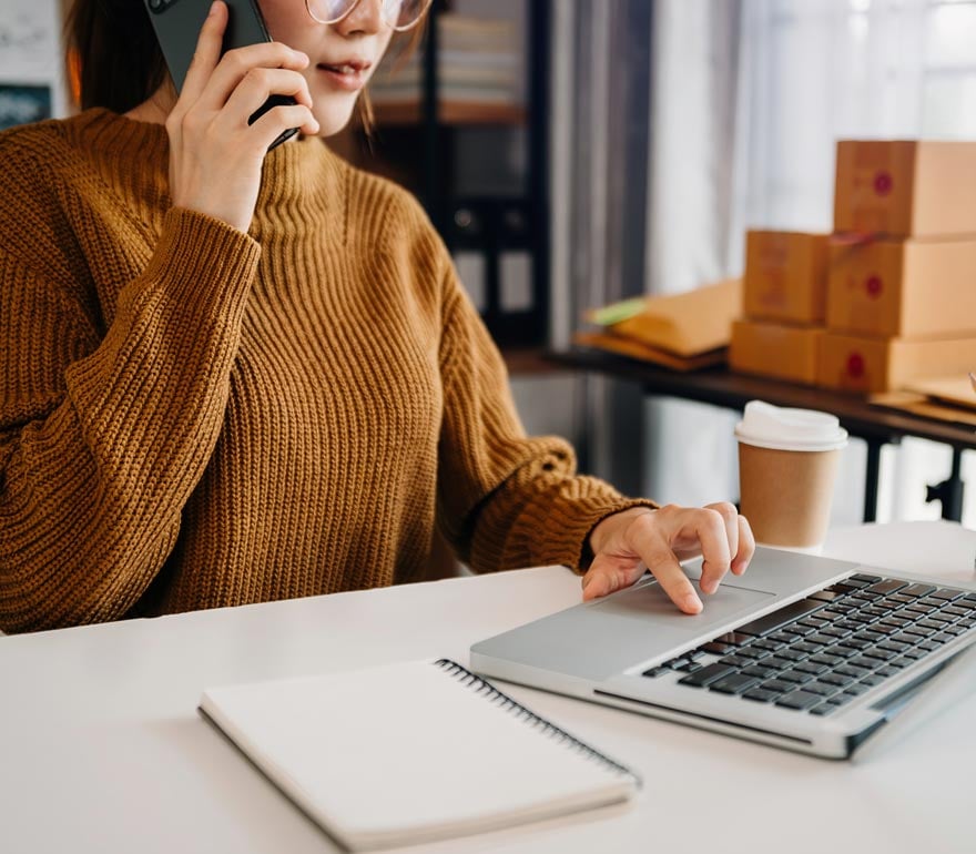 Small business owner in her office on her phone laptop navigating compliance with expert support