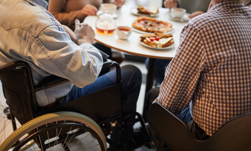 Person in wheelchair enjoying a meal at a restaurant with a group