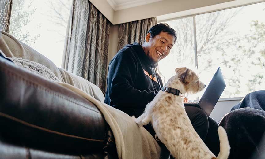 a male employee working remotely and smiling at his dog