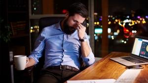 White-collar worker looking tired at his desk, representing working overtime 