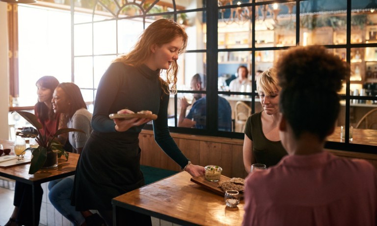 Tipped employee serving food to a table of smiling customers