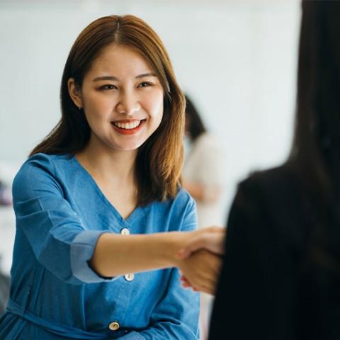 two woman handshaking and smiling in an office setting