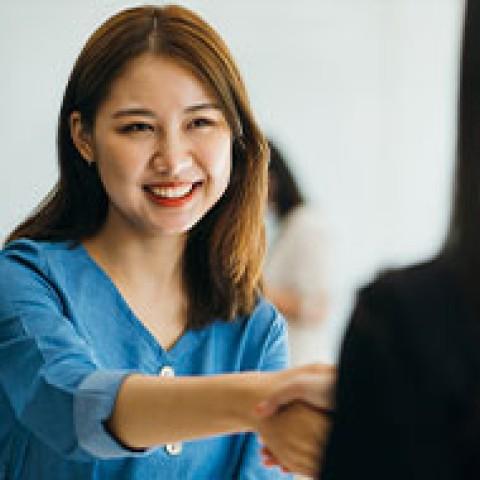 dark-haried woman in blue shirt shakes hand of dark-haired woman she faces