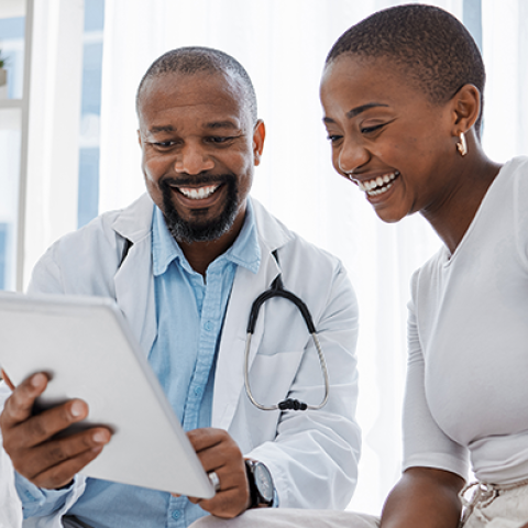 Smiling doctor shows a tablet to a patient during a friendly consultation in a medical office.