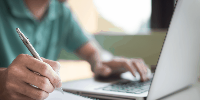 man on a computer and taking notes on a notepad
