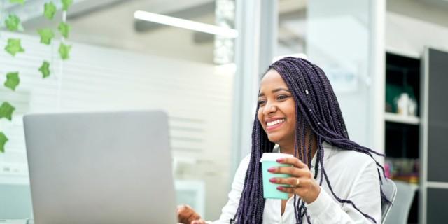 Mujer sentada frente a una computadora con un café en la mano