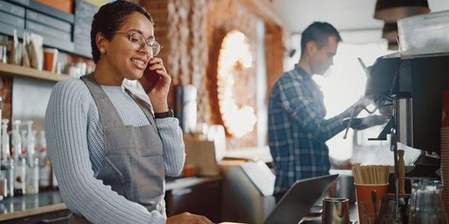 propietario de una pequeña empresa hablando por teléfono y revisando ua computadora portátil