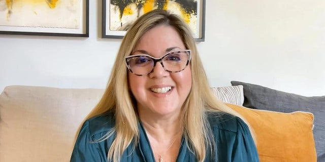 blonde woman with glasses and emerald green shirt sits on orange couch