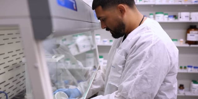 pharmacist fills bottles behind glass screen