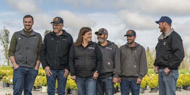 multiple generations of the Fessler family of Oregon stand laughing amid nursery plantings