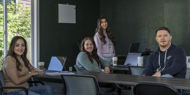 group of employees smile from positions around an office with dark gray walls