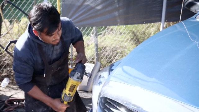 An employee at an auto body shop works on  preparing a vehicle to be painted.