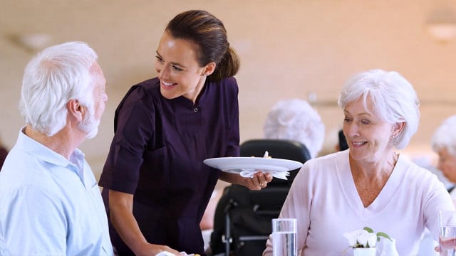 Un empleado de Discovery Senior Living ayuda a los residentes con sus comidas.