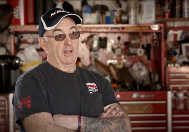 man in sunglasses and ballcap stands in front of repair tools