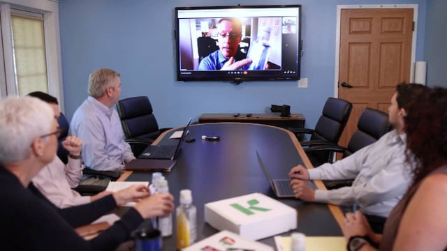staff team at table meets virtually with others onscreen