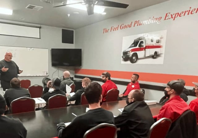 man speaks at front of room training team at plumbing MD in CA