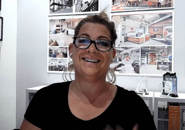 propietaria de un estudio de diseño arquitectónico sonríe frente a una pared con muestras de proyectos