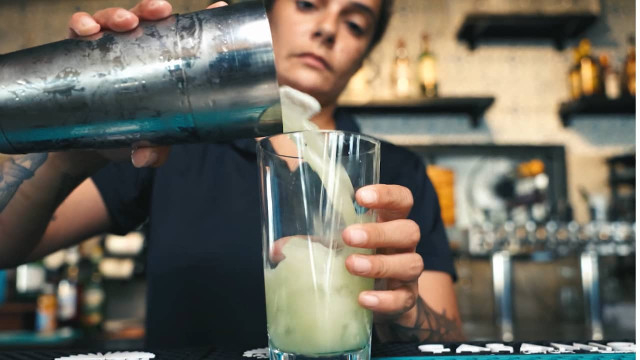 bartender pours mixed drink into glass