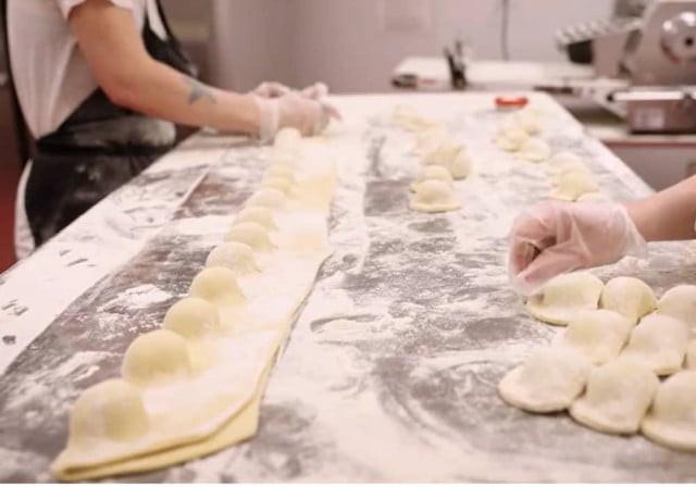 two culinary workers hands shape rows of pierogis on long table