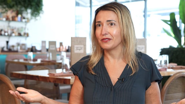 blond-haired woman sits and gestures in restaurant setting