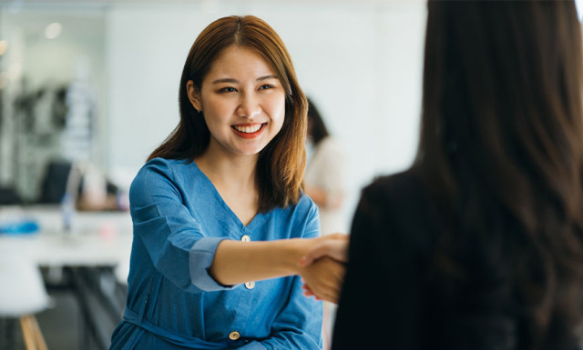 two woman handshaking and smiling in an office setting