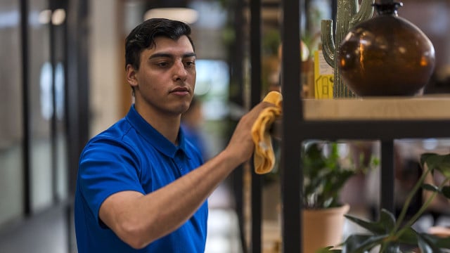 An employee of City Wide Facility Solutions works at dusting the shelves at a client's office.
