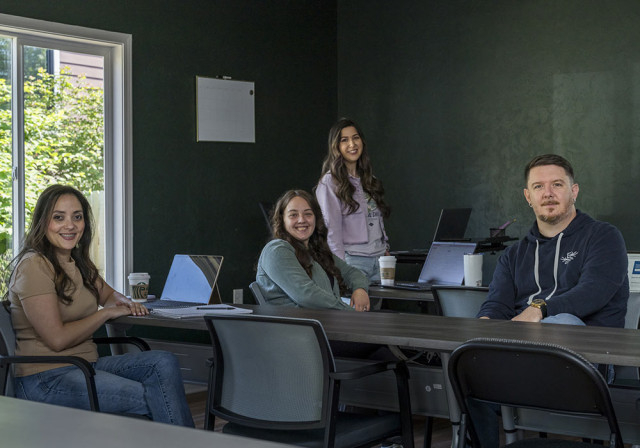group of employees smile from positions around an office with dark gray walls