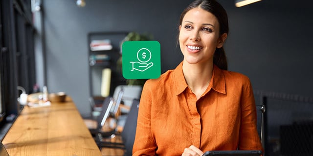 A person stands in a modern workspace holding a tablet, with a floating green icon showing a hand and dollar symbol beside them.