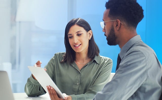 Two people seated at a desk review information on a tablet together in a bright modern office.