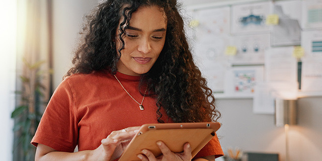 Curly-haired woman inside a room works on an electronic tablet